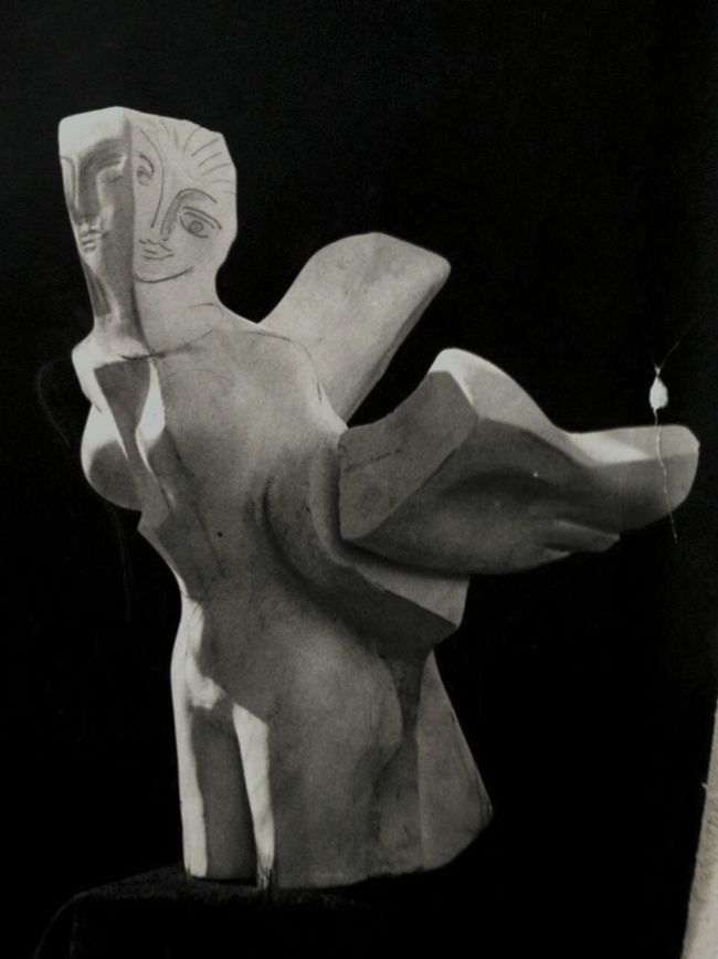 Alabaster sculpture “Archeology”: a light stone female torso with a carved face and two angular wing-like forms, photographed in black and white against black.