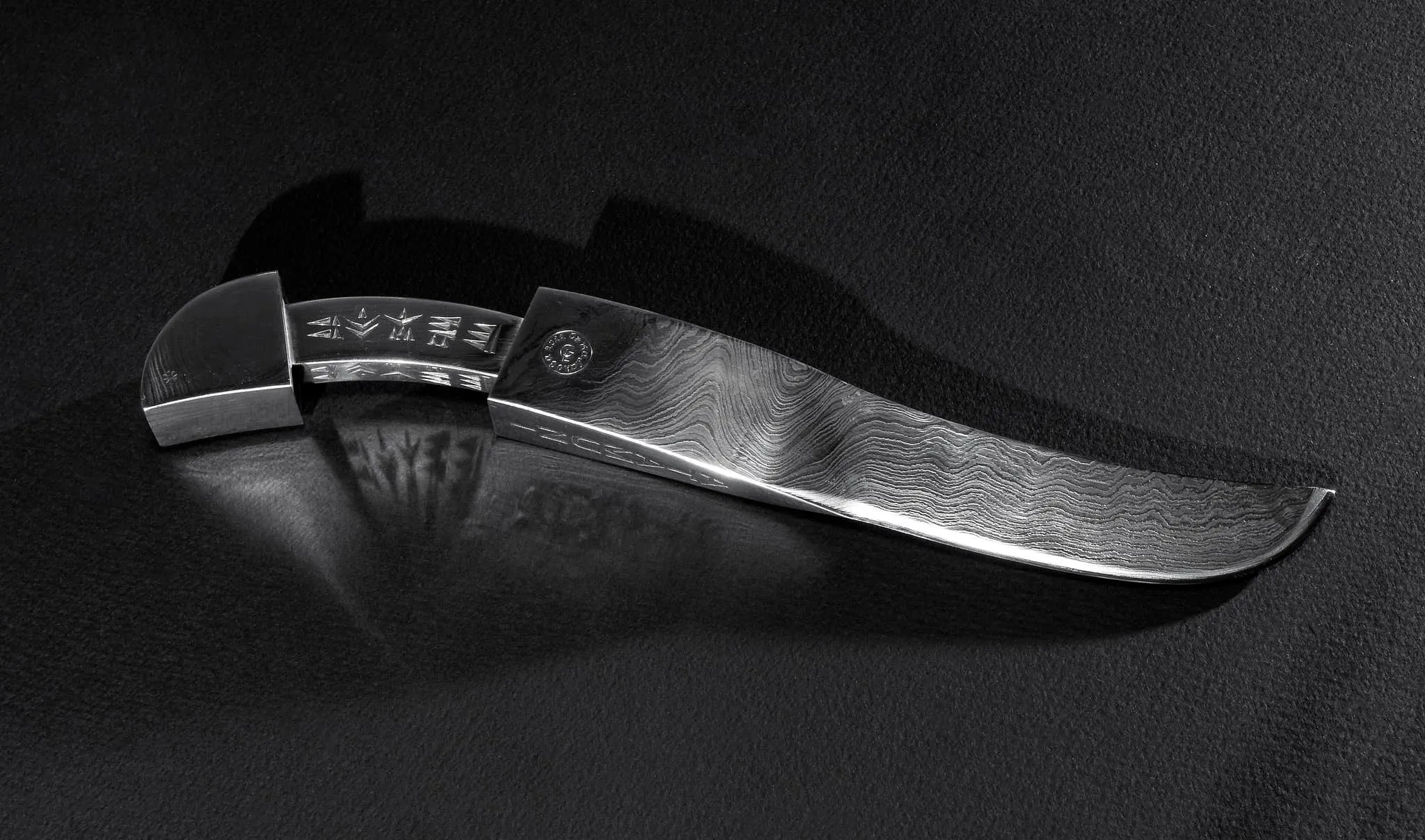 Finished Atamuni knife with patterned steel blade and engraved handle on a black surface