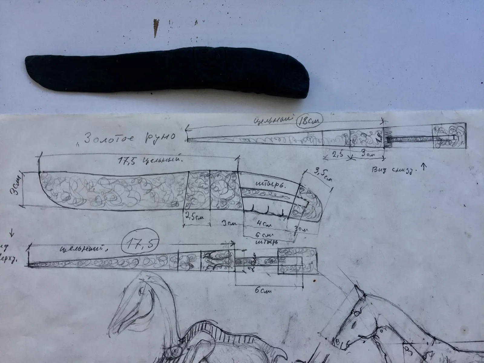 Dark plasticine model of a knife above pencil sketches with dimensions and drawings of horses