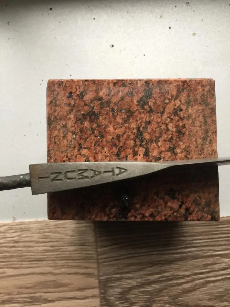 Engraved blade of the knife lying across a block of red granite