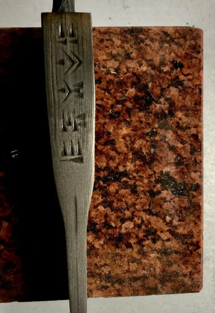 Knife blade with engraved cuneiform-like signs lying on red granite