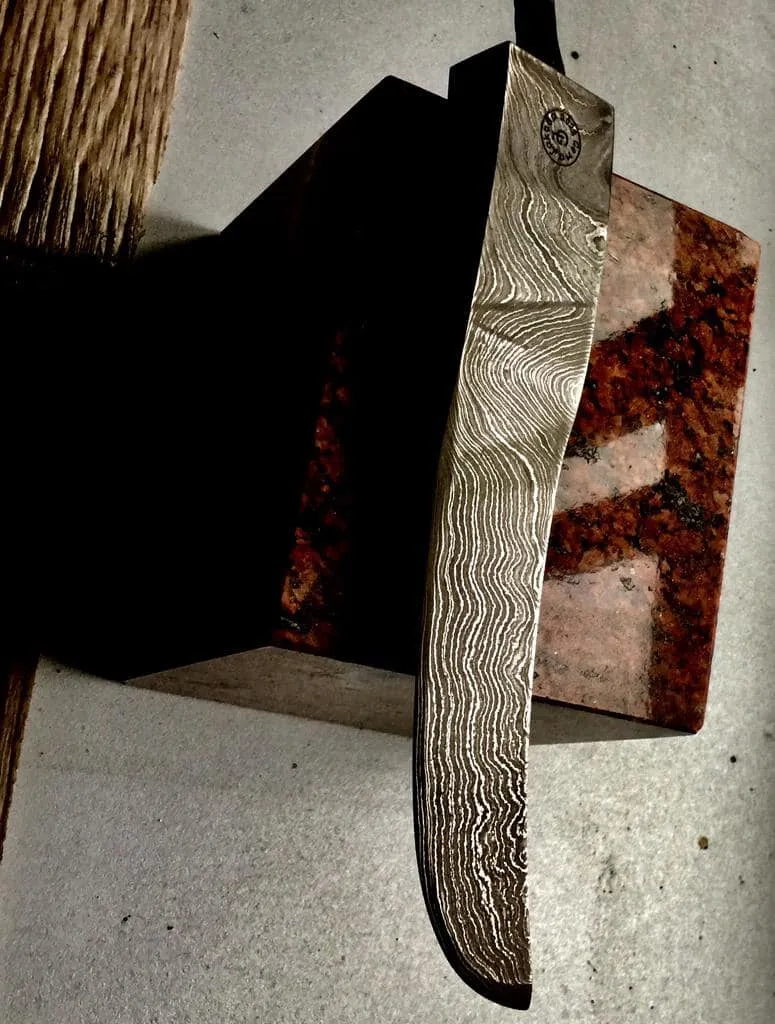 Knife blade with patterned Damascus-style steel resting on red granite