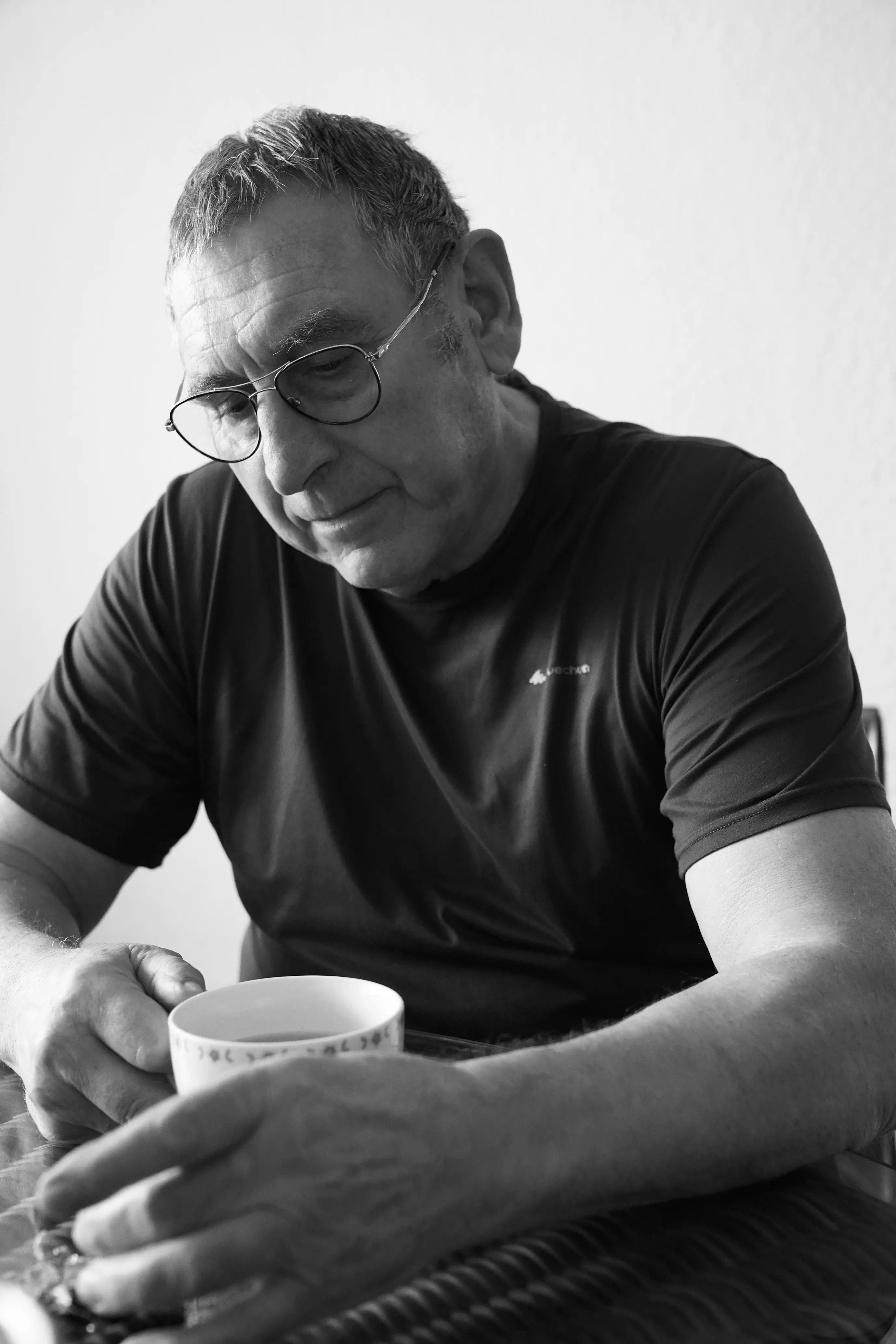 Portrait en noir et blanc de l’artiste assis, portant des lunettes et tenant une tasse
