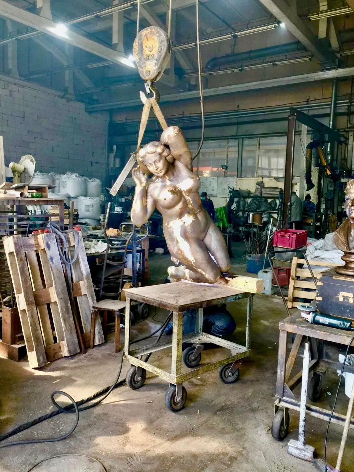 Cast figure suspended from a hoist over a trolley in the foundry