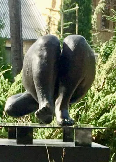 Rear view of the bronze figure’s legs on the glass sheet, outdoors