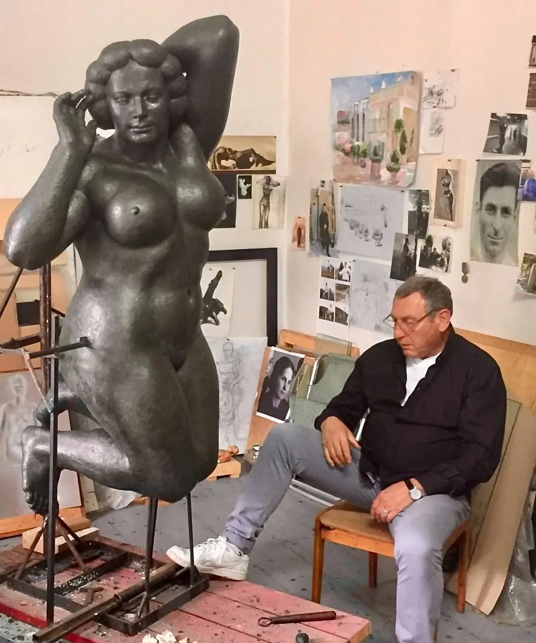 Margo in plasticine, standing on a metal frame, with the sculptor seated beside it in the studio