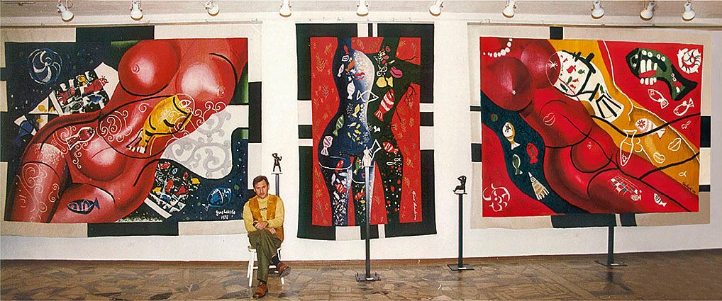 Triptych of tapestries “Life Waters” hanging in a gallery: two red reclining nude figures with fish on either side of a tall blue-and-green figure, the artist seated below.