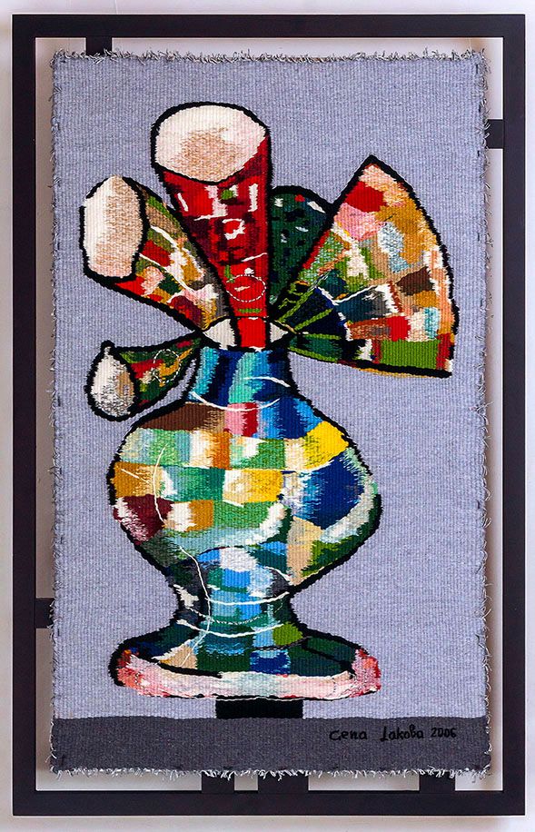 Tapestry “Vase with the flowers - 1”: a patchwork-coloured vase with large fan-shaped red and green flowers, on a pale blue-grey background, in a dark frame.